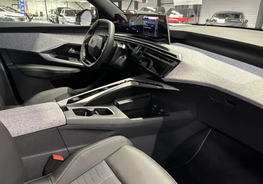 Vue intérieure côté conducteur du Peugeot 3008 Hybrid 2025, avec tableau de bord gris clair et écran panoramique incurvé.