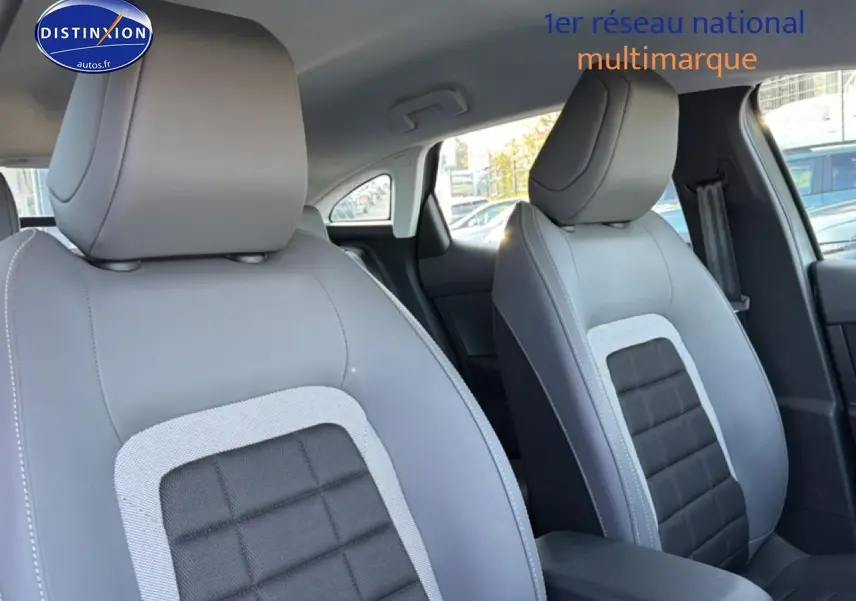 Gros plan sur les sièges avant gris clair et noir de la Citroën C4 électrique 2025, avec accoudoir central visible.