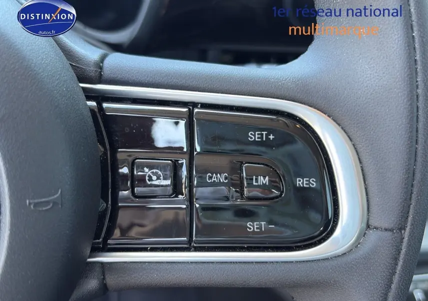 Gros plan sur les commandes du régulateur de vitesse au volant noir de la Fiat 500 électrique blanche MY23.