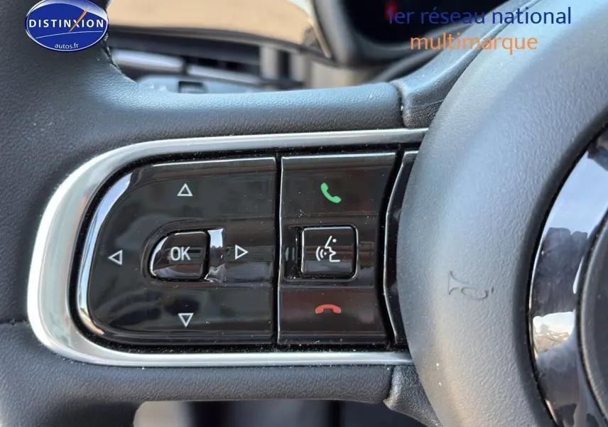 Gros plan sur les commandes multifonctions noires du volant de la FIAT 500 e blanche, version 2024.