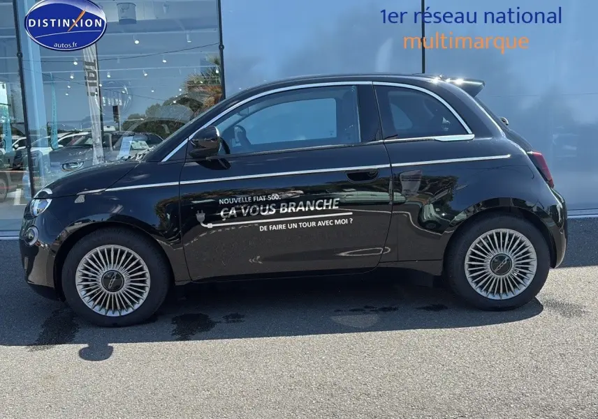 Profil côté gauche de la Fiat 500 électrique noire 2024 avec jantes alu et lettrage publicitaire sur la porte.