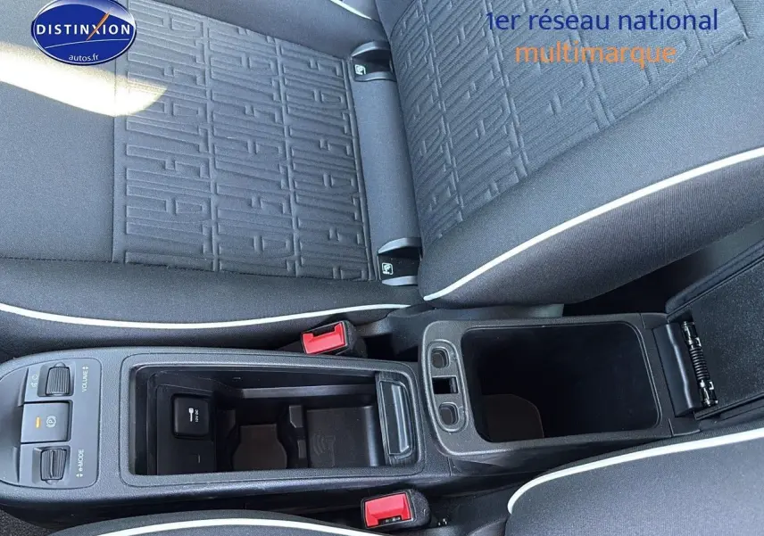 Vue plongeante sur la console centrale noire et les sièges tissu noir avec surpiqûres blanches d'une Fiat 500 électrique blanche.
