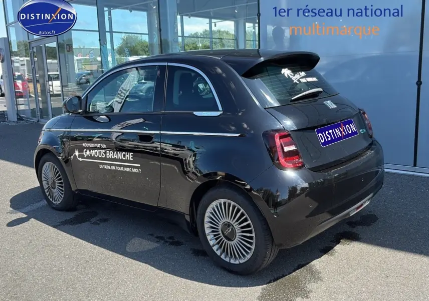 Vue 3/4 arrière droite d'une Fiat 500 électrique noire avec jantes alu et stickers publicitaires sur la porte.