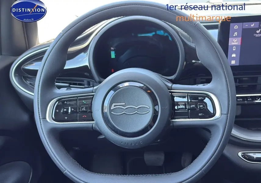 Vue rapprochée du volant multifonction noir de la FIAT 500 électrique blanche, avec tableau de bord numérique et écran tactile.