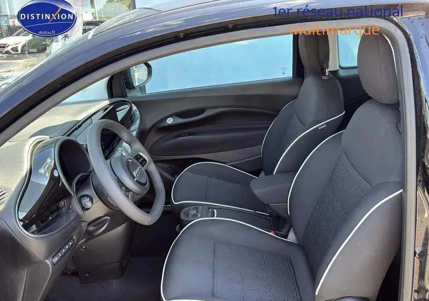 Intérieur de la Fiat 500 électrique 2024 vu côté gauche, sièges noirs avec surpiqûres blanches et volant multifonction.