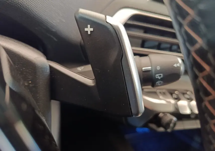 Gros plan sur la palette de changement de vitesse "+" côté droit du volant dans l'habitacle d'un Peugeot 5008 gris clair.