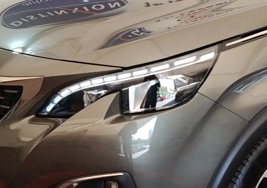 Gros plan sur le phare avant droit du Peugeot 5008 gris clair, mettant en valeur les LED distinctives et la carrosserie lisse.