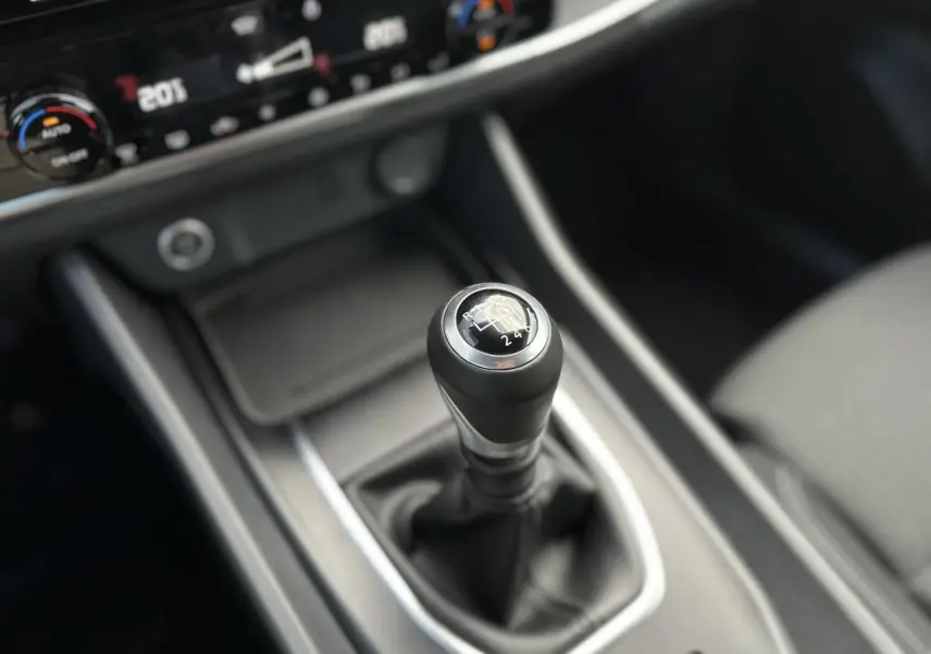Gros plan sur le levier de vitesses manuel noir du Nissan Qashqai 2025, avec console centrale et commandes de climatisation visibles.