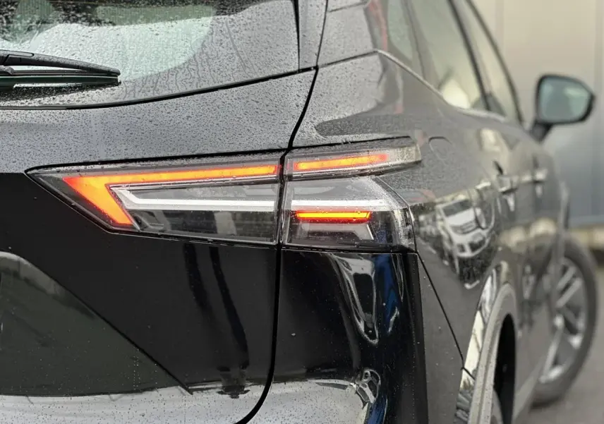 Feu arrière droit allumé d’un Nissan Qashqai noir nacré vu en gros plan sous la pluie, avec reflet sur la carrosserie.