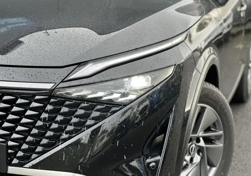 Gros plan sur l'avant droit du Nissan Qashqai noir nacré 2025, mettant en valeur le phare LED et la calandre texturée.