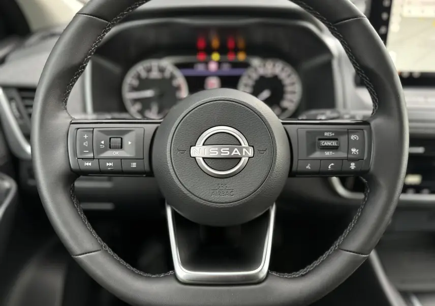 Gros plan sur le volant noir du Nissan Qashqai 2025 avec commandes intégrées et tableau de bord flou en arrière-plan.