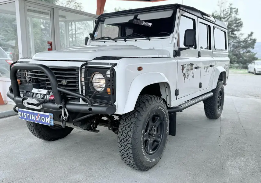Land Rover Defender blanc vu 3/4 avant droit avec pare-buffle noir et pneus tout-terrain marqués BFGoodrich.