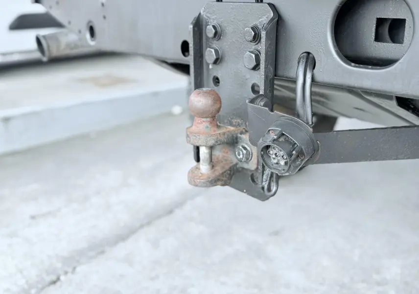 Gros plan sur l'attelage arrière rouillé et la prise électrique noire du Land Rover Defender blanc de 2007.