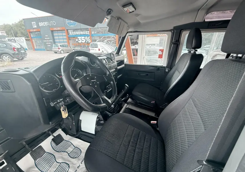 Vue intérieure côté conducteur du Land Rover Defender 2.4 TD4 2007 avec sièges tissu gris-noir et volant sport noir.