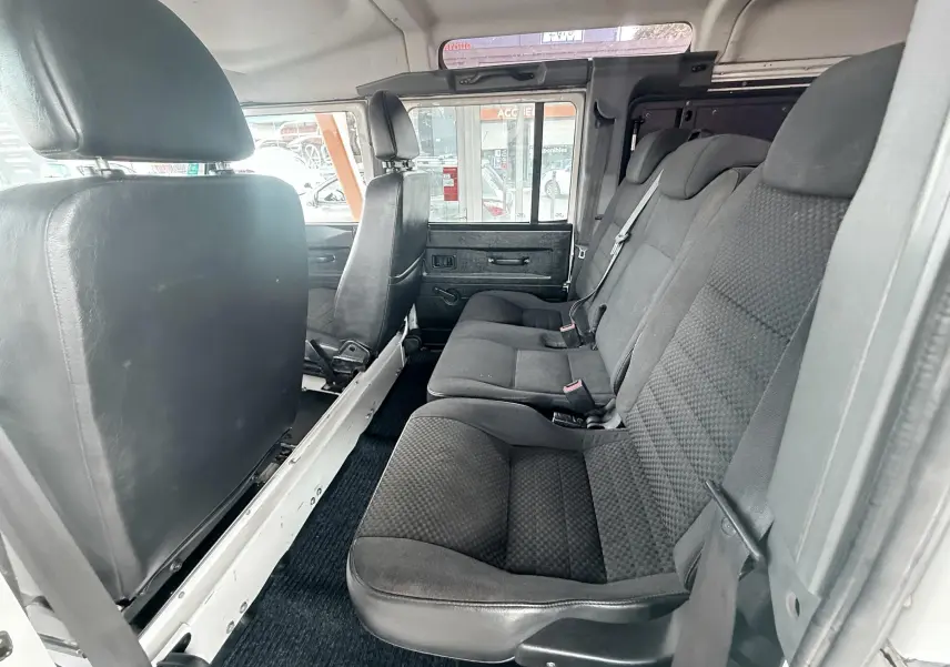 Vue intérieure côté droit du Land Rover Defender blanc 2007, montrant les sièges arrière en tissu gris noir et la porte ouverte.