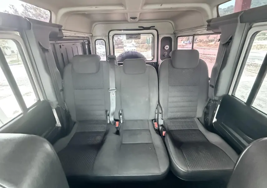 Vue intérieure arrière du Land Rover Defender 2007 montrant les sièges en tissu gris-noir et les fenêtres latérales.