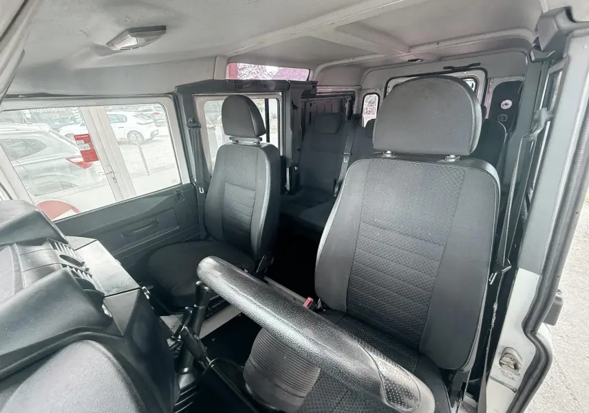 Vue intérieure côté conducteur du Land Rover Defender blanc de 2007, montrant les sièges en tissu gris-noir et le volant.