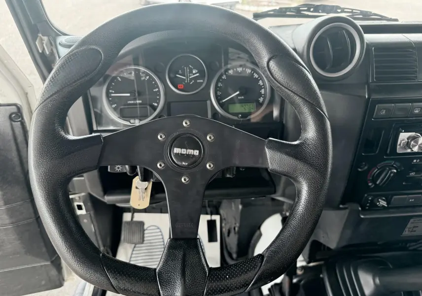 Vue intérieure centrée sur le volant sport noir Momo du Land Rover Defender 2007 avec tableau de bord gris et commandes visibles.
