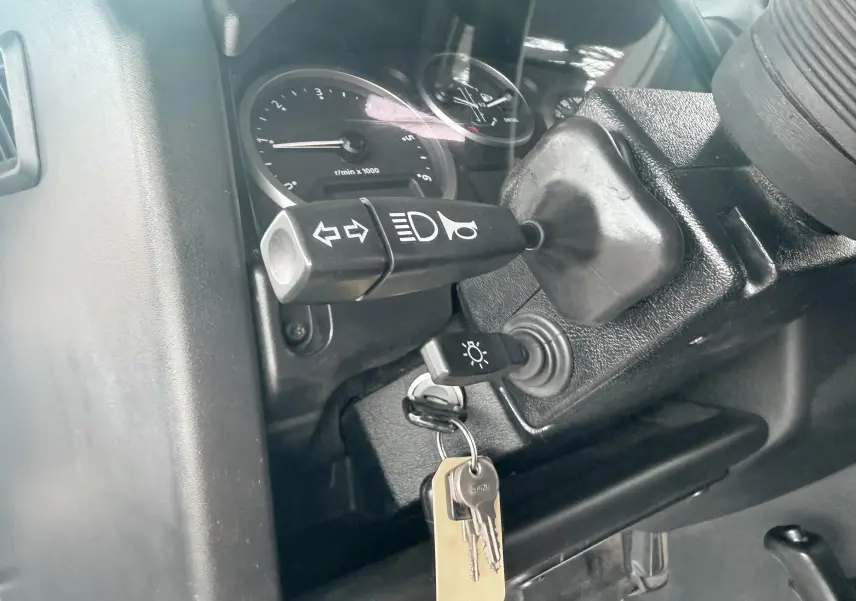Gros plan sur la colonne de direction du Land Rover Defender blanc, montrant les commandes de clignotants et le contact avec clés.