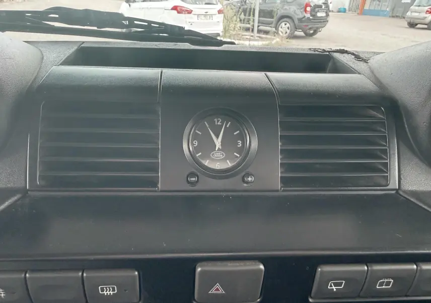 Gros plan sur l'horloge centrale et les aérateurs noirs du tableau de bord intérieur du Land Rover Defender blanc de 2007.
