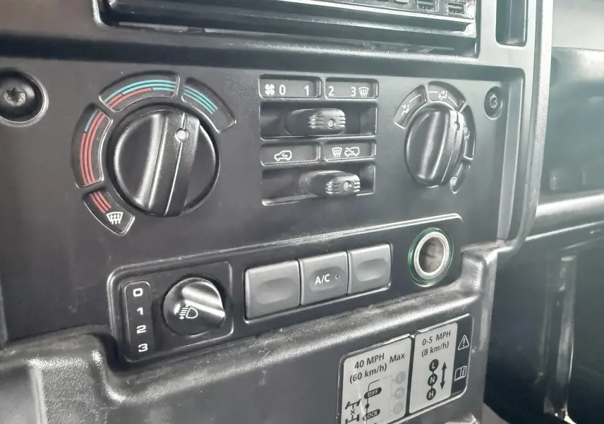 Gros plan sur la console centrale du Land Rover Defender 2007, montrant les commandes de climatisation et ventilation en plastique noir.