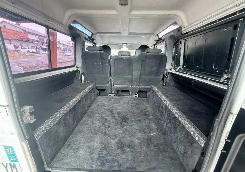 Vue intérieure arrière du Land Rover Defender blanc 2007, montrant l’espace de chargement avec banquettes rabattues et revêtement noir.