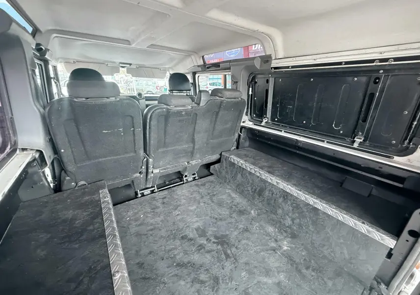 Vue intérieure arrière du Land Rover Defender blanc 2007, montrant les sièges arrière et l'espace de chargement aménagé.