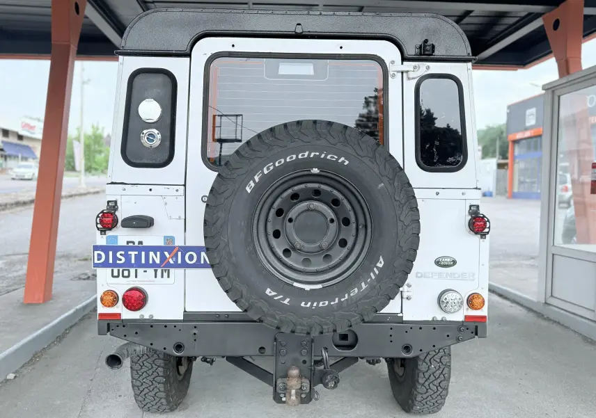 Vue arrière d'un Land Rover Defender blanc 2007 avec roue de secours BFGoodrich et attelage visible.