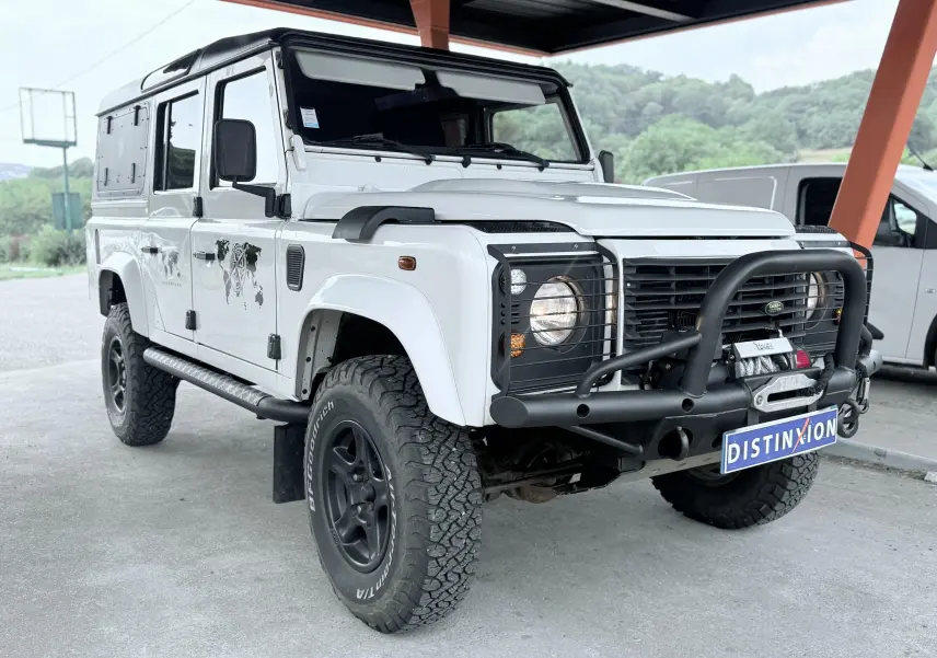 Land Rover Defender blanc vue 3/4 avant droit avec pare-buffle noir et pneus tout-terrain marqués BFGoodrich.