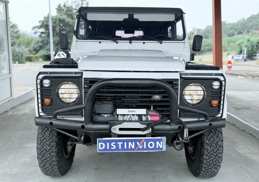 Vue avant d'un Land Rover Defender blanc de 2007 avec pare-buffle noir et treuil intégré, phares allumés.