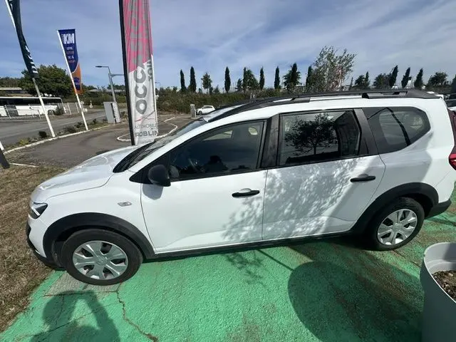 Vue de profil côté gauche d'un Renault Dacia Jogger blanc 2023, avec barres de toit et jantes acier.