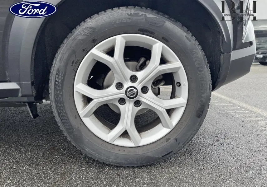 Gros plan sur la roue avant droite d'un Nissan Juke noir métallisé avec jante alu à design moderne.