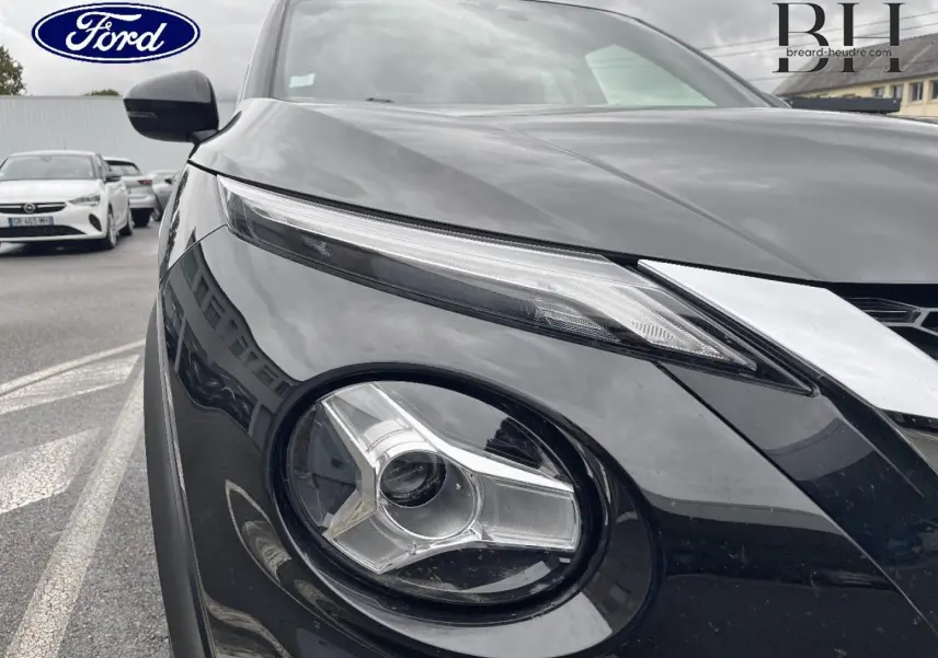 Gros plan sur le phare avant gauche du Nissan Juke noir métallisé, mettant en valeur son design distinctif et moderne.