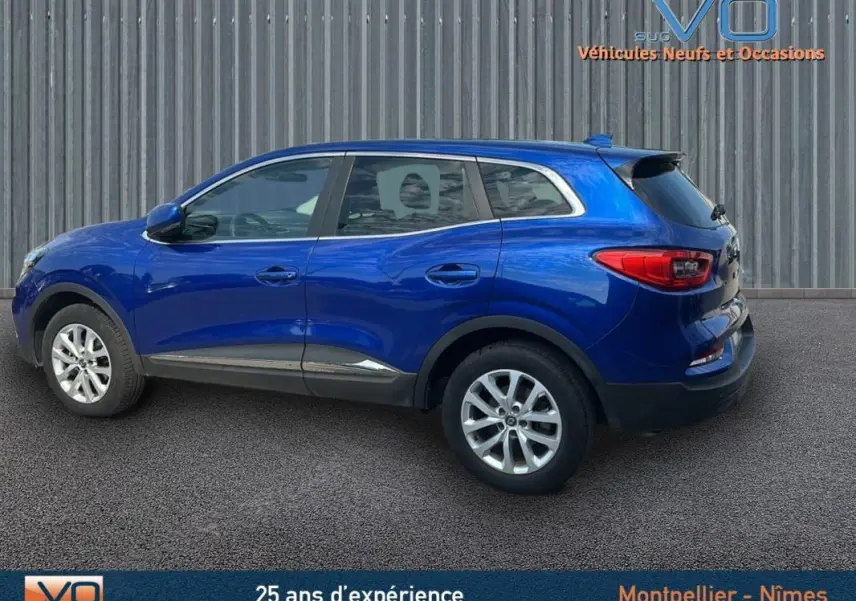 Profil latéral droit d'un Renault Kadjar TCe 140 bleu foncé avec jantes alliage et barres de toit visibles.