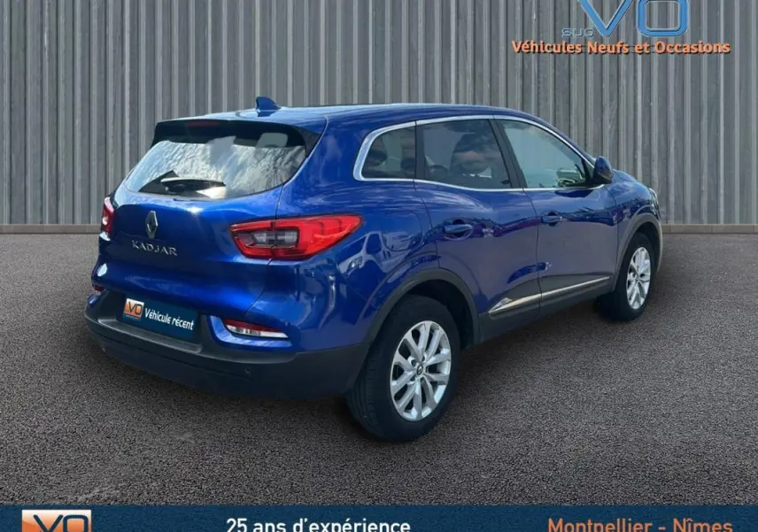 Vue 3/4 arrière droite d'un Renault Kadjar bleu foncé avec barres de toit et jantes alliage 17 pouces sur parking.