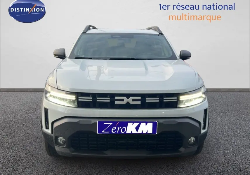 Vue frontale du Dacia Duster 2025 blanc glacier avec calandre noire et feux LED allumés sur fond neutre.