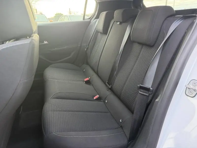 Vue intérieure côté droit des sièges arrière noirs de la Peugeot 308 2024 en blanc Okénite, avec ceintures de sécurité visibles.