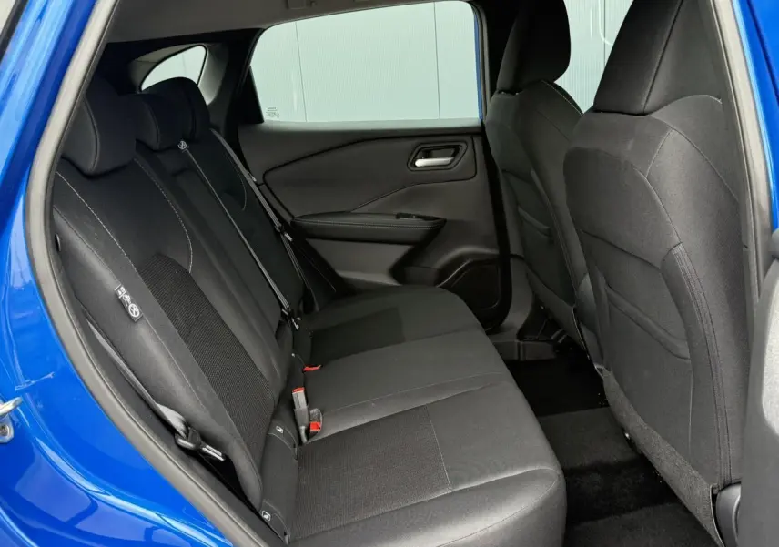 Vue intérieure côté gauche des sièges arrière noirs du Nissan Qashqai III bleu magnétique avec ceinture de sécurité visible.