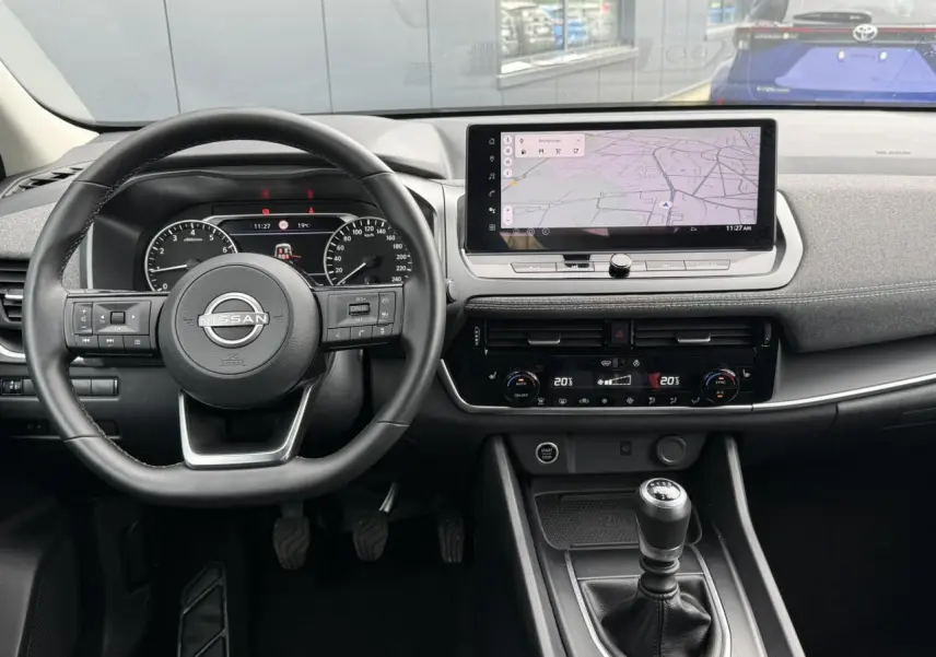Vue intérieure du tableau de bord du Nissan Qashqai 2025, avec volant, écran tactile et levier de vitesses manuelle.