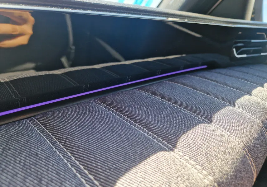 Gros plan intérieur sur la planche de bord de la Renault R5 E-TECH 2025 avec éclairage d’ambiance violet et tissu gris texturé.