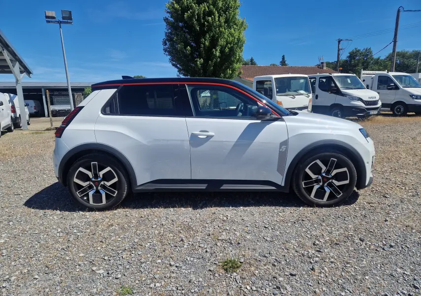 Profil droit de la Renault R5 E-TECH 2025 blanc nacré avec toit noir et jantes stylisées sur un parking extérieur.