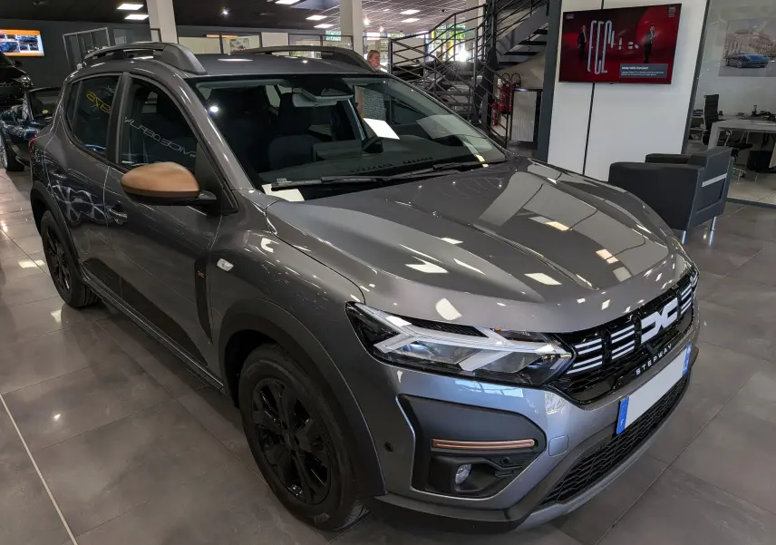 Vue 3/4 avant droite d'une Dacia Sandero Stepway TCe 110 Gris Schiste avec rétroviseurs couleur cuivre en showroom.