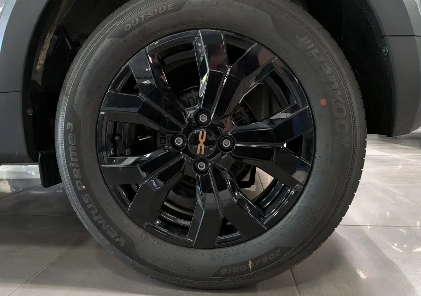 Gros plan sur la roue avant droite de la Dacia Sandero Stepway 2025, jante noire brillante avec logo orange au centre.