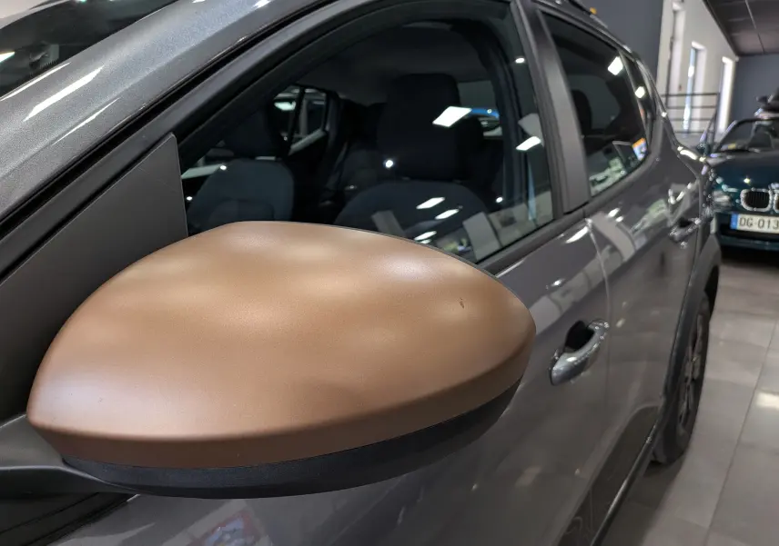 Gros plan sur le rétroviseur droit bronze du Dacia Sandero Stepway gris schiste, vue latérale en intérieur showroom.
