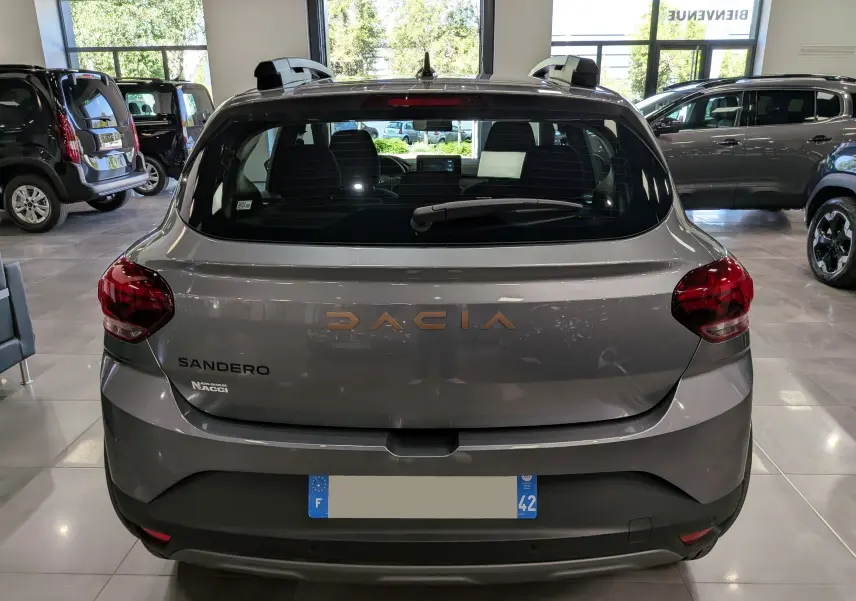 Vue arrière d'une Dacia Sandero Stepway gris schiste en showroom, avec logo Dacia et feux arrière rouges visibles.