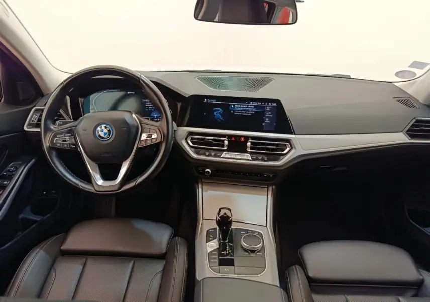 Vue intérieure avant de la BMW Série 3 320e hybride, tableau de bord noir avec écran tactile et volant cuir multifonctions.