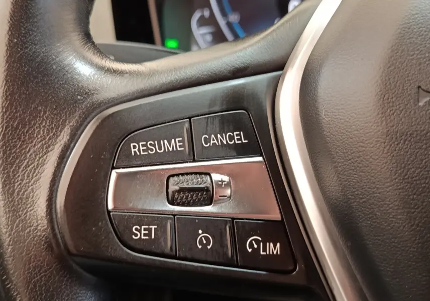 Gros plan sur les commandes de régulateur de vitesse au volant cuir noir de la BMW Série 3 320e hybride.