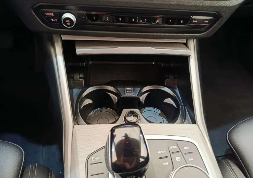 Vue rapprochée de la console centrale noire et argentée de la BMW Série 3 320e hybride avec sélecteur de vitesse et porte-gobelets.