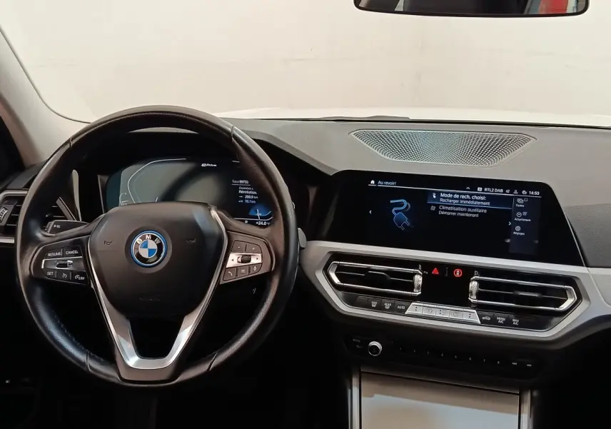 Vue intérieure frontale du tableau de bord et volant noir de la BMW Série 3 320e hybride, avec écran tactile et commandes intégrées.