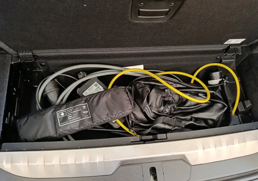 Coffre ouvert d’une BMW Série 3 hybride blanche, vue plongeante sur câbles de recharge et accessoires rangés.